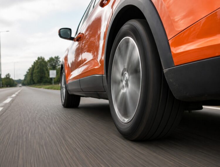 Oranje auto rijdt zuinig over de weg met focus op de banden
