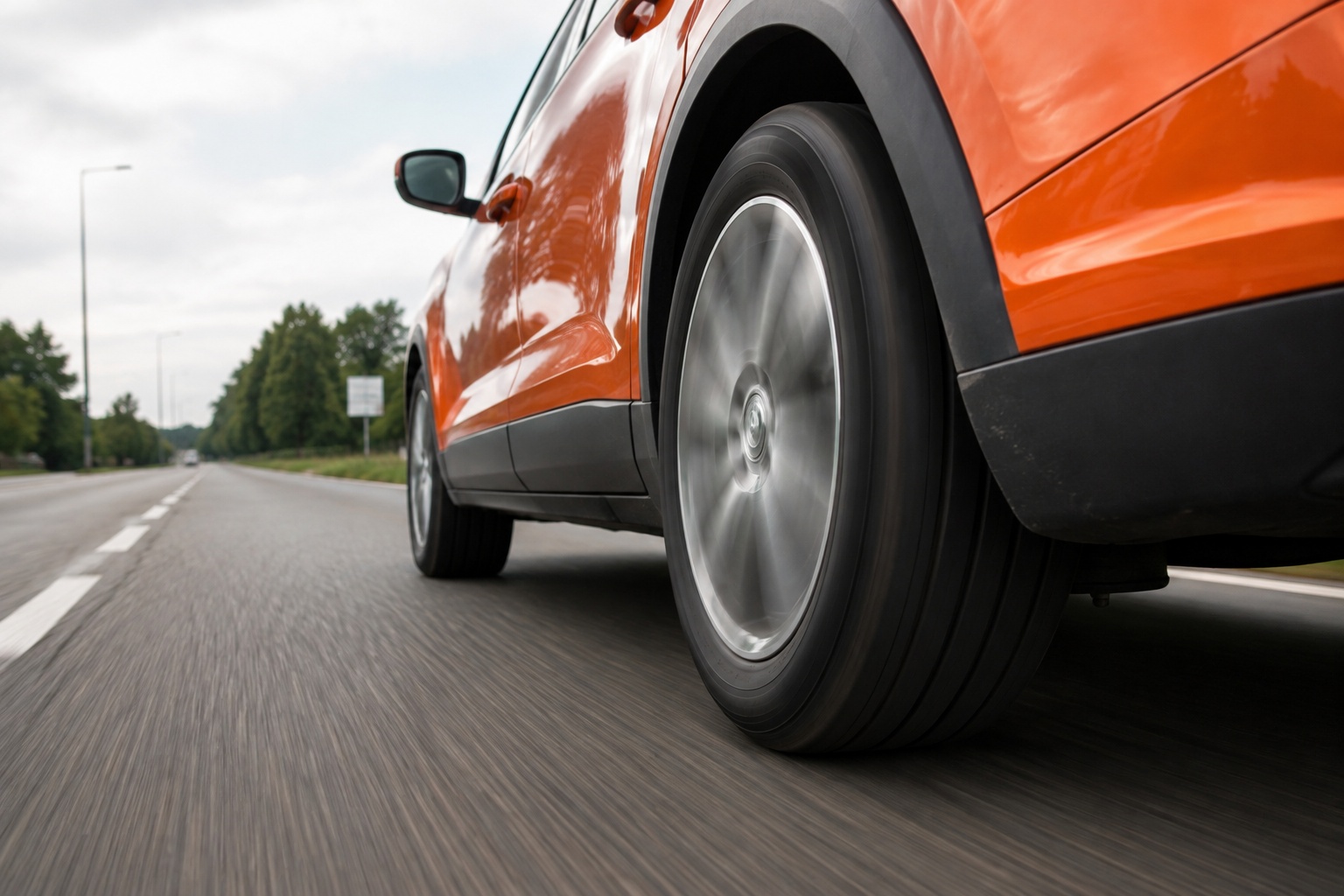 Oranje auto rijdt zuinig over de weg met focus op de banden