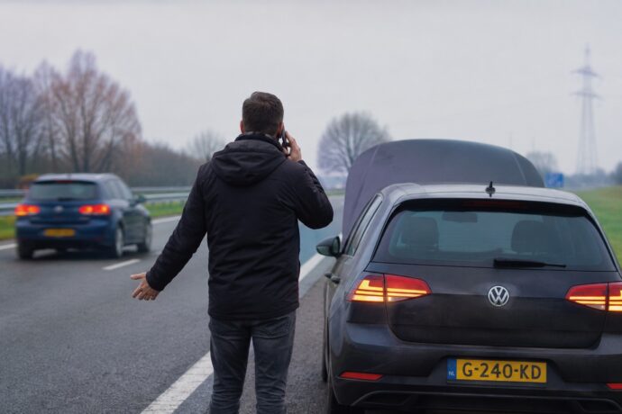 Automobilist met pech belt om hulp naast een auto met Nederlands kenteken